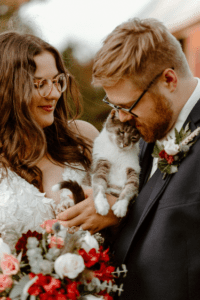 married couple wearing glasses posed with cat in their arms