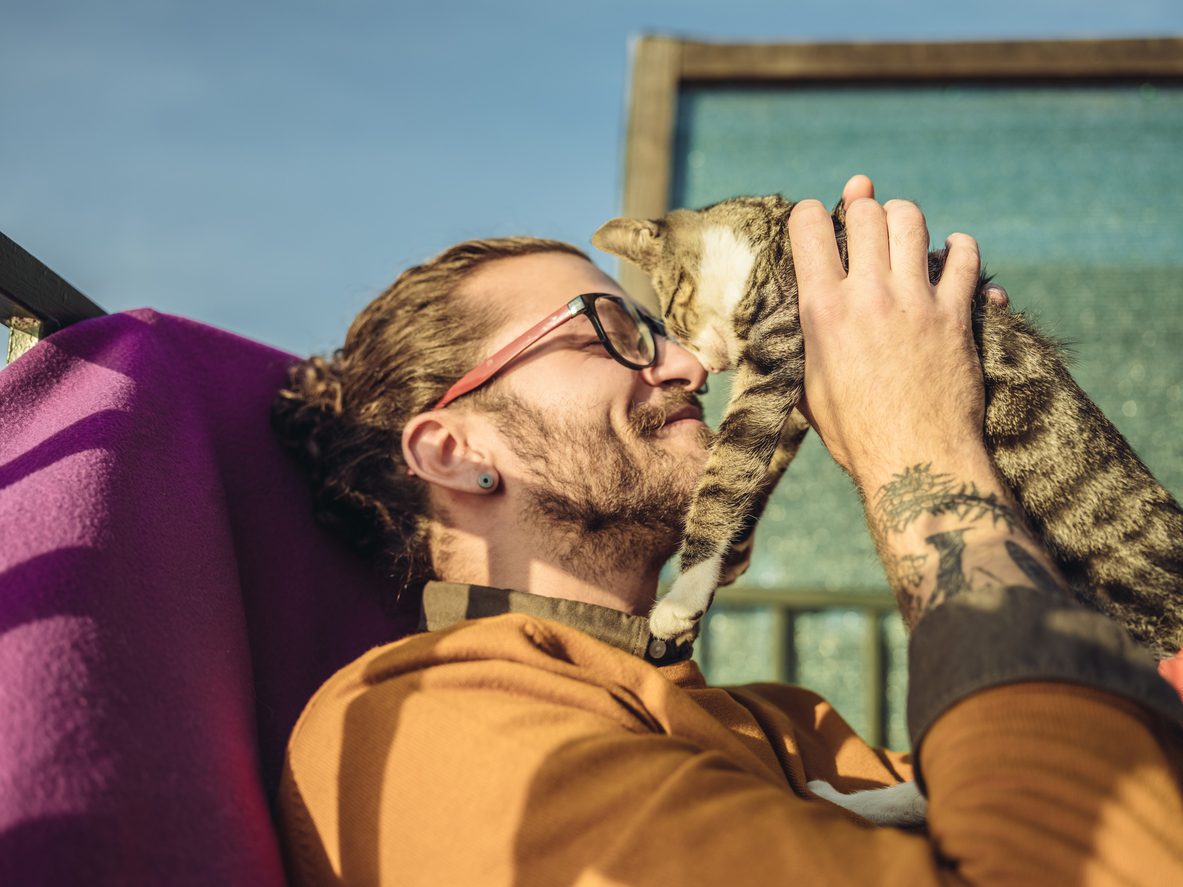Millennial man cuddling with tabby cat outdoors